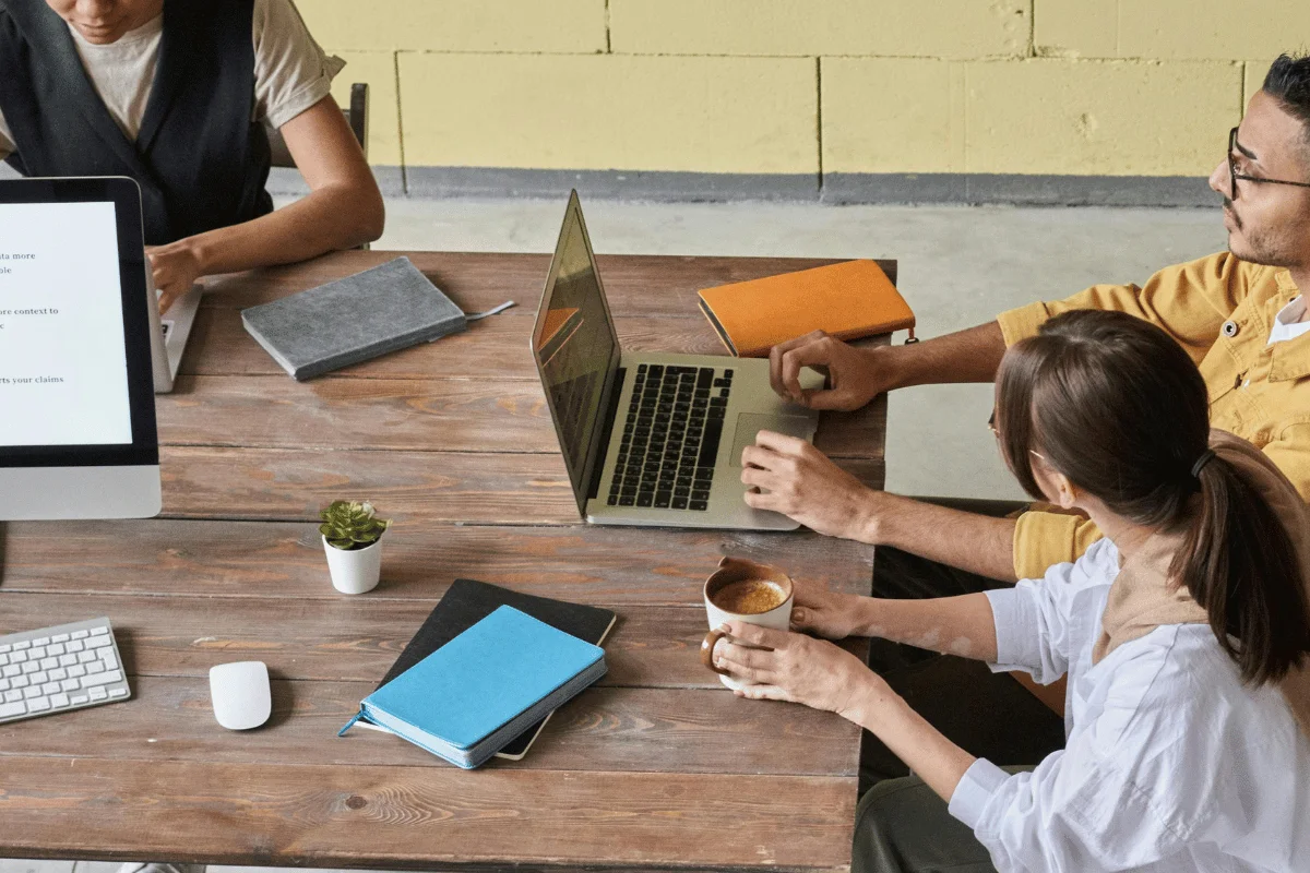 Group collaborating at a shared workspace with coffee and notebooks.