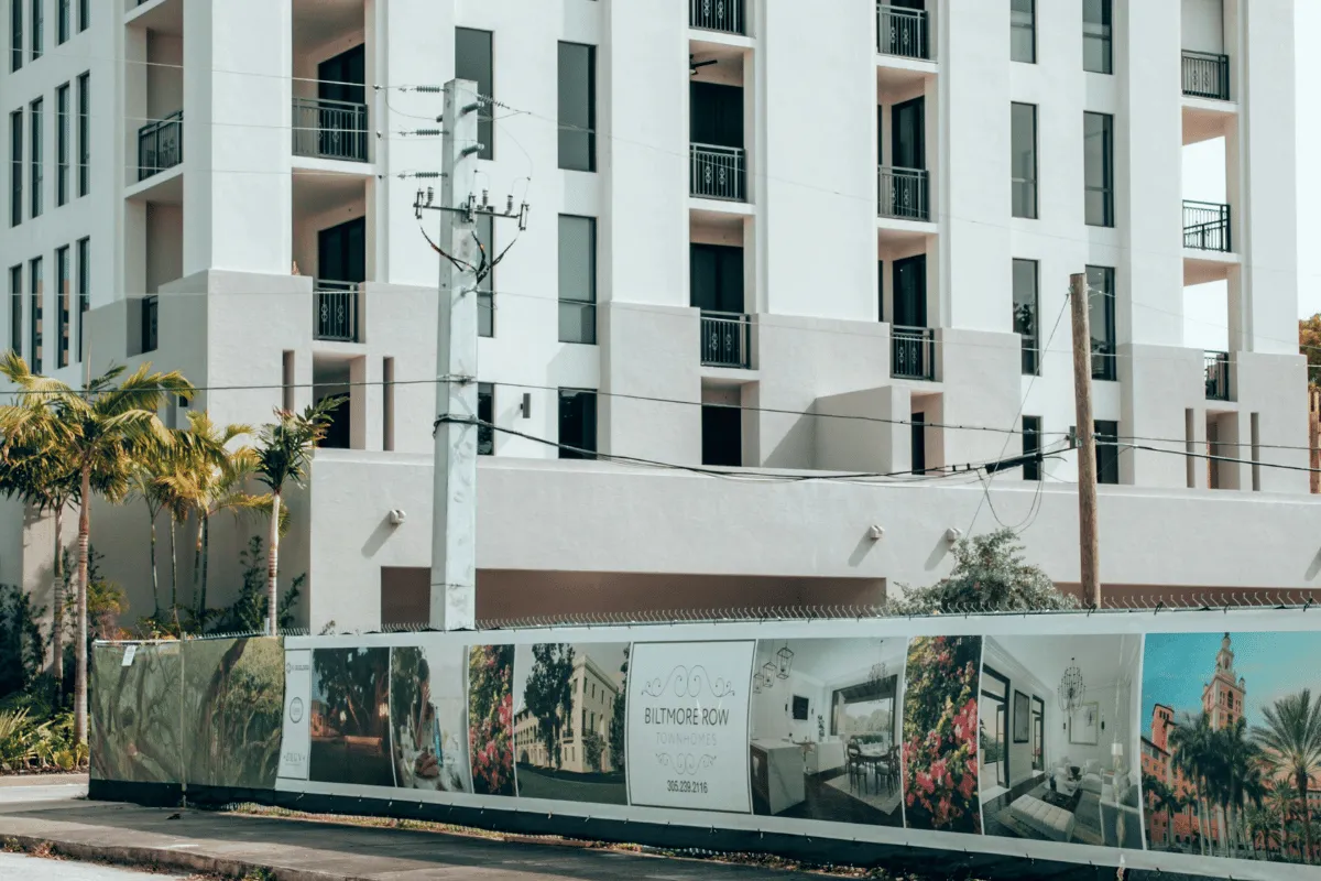A newly constructed building with a promotional fence showcasing luxury townhomes for sale.