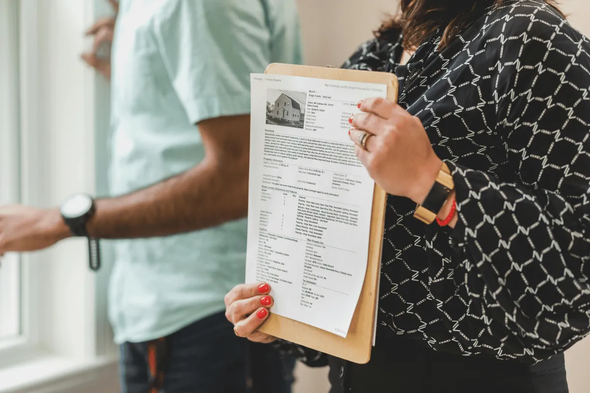 A woman holding a real estate listing document while standing next to a man in a property showing.