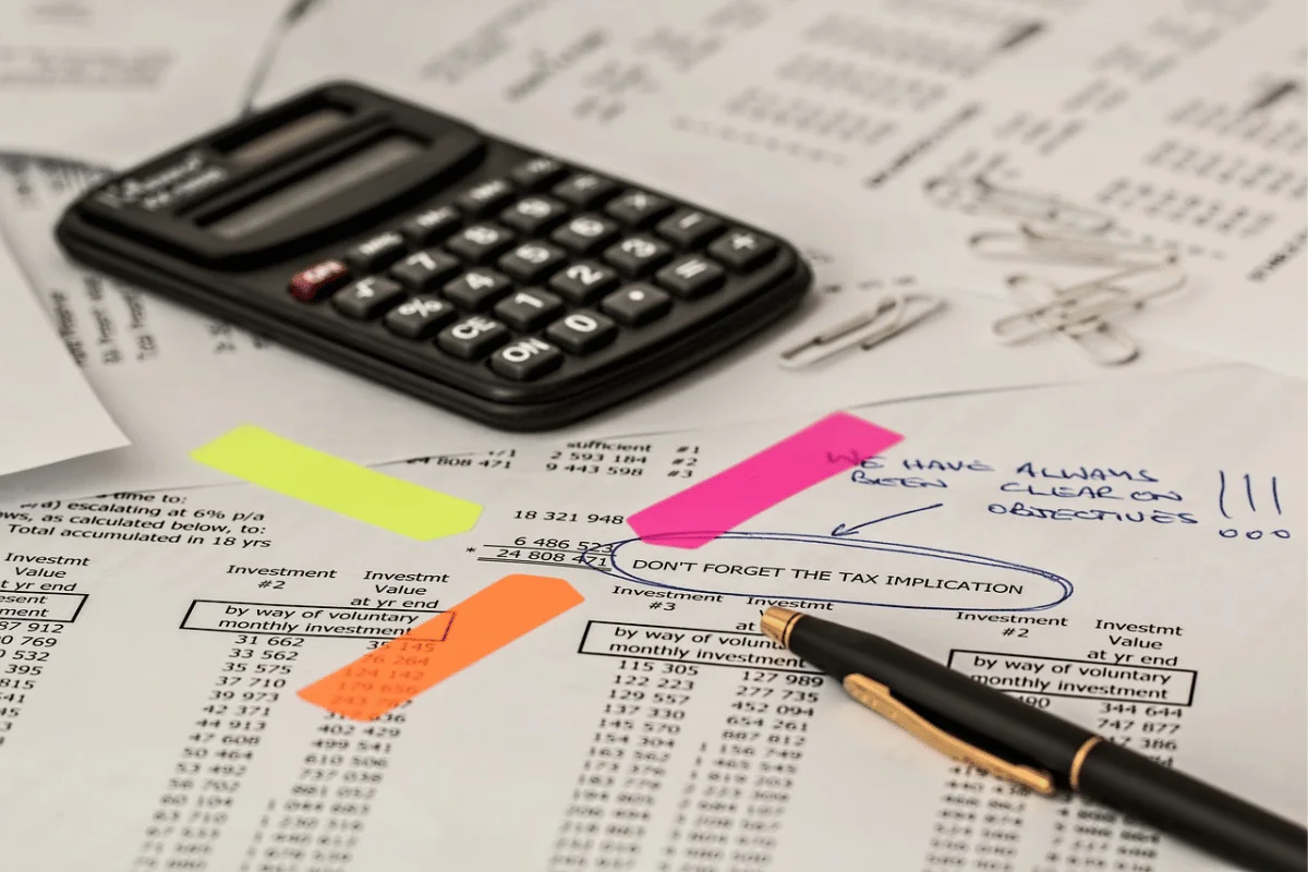 An overhead shot of financial statements with various highlighter marks, a calculator, and a pen.