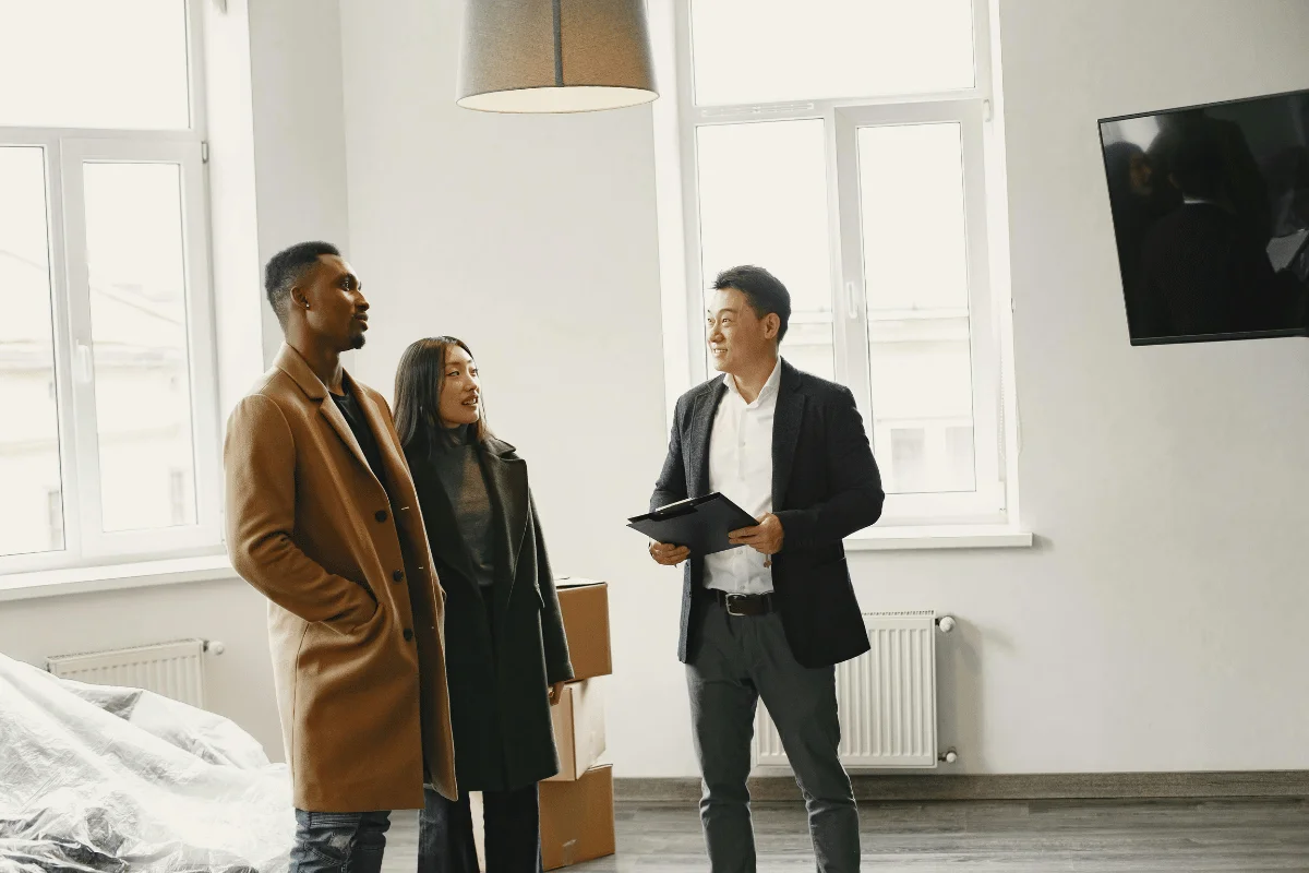 A couple in winter coats discussing the layout of a bright and spacious apartment with a real estate agent.