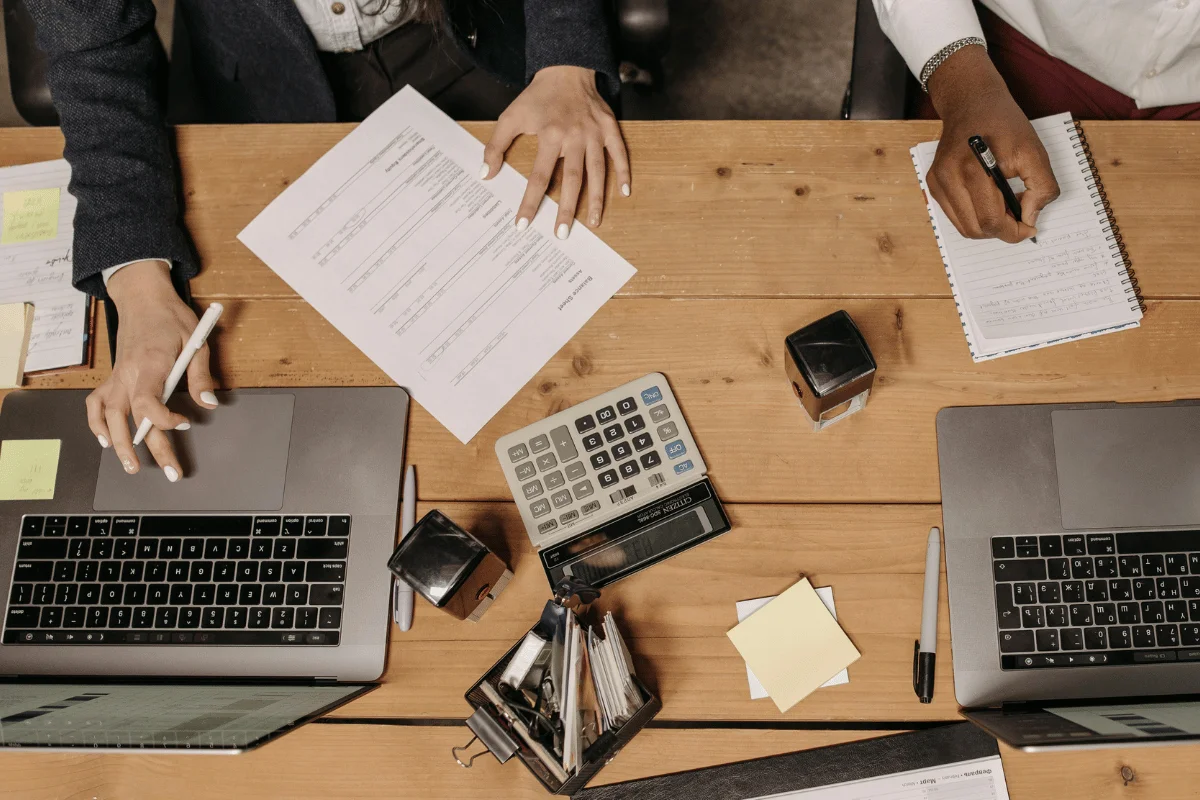 Business meeting with paperwork, calculator, and laptops on desk.