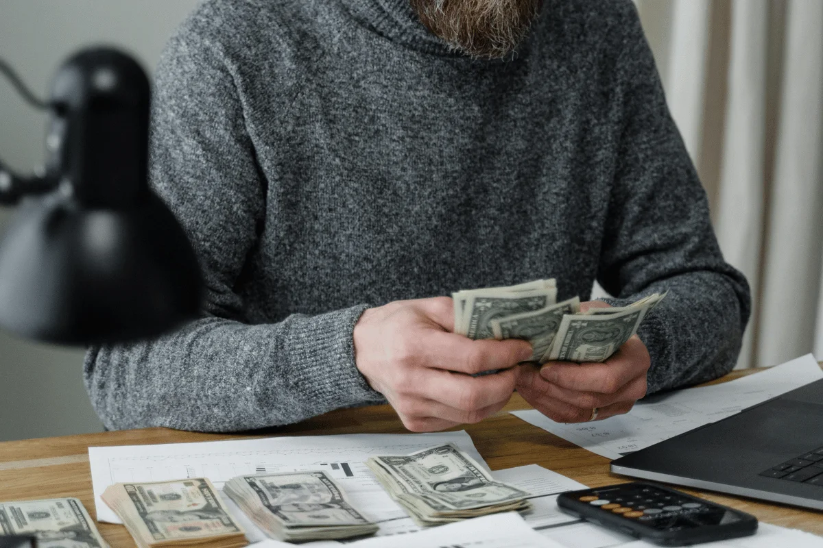 Someone organizing money on a wooden desk with a calculator and paperwork nearby.