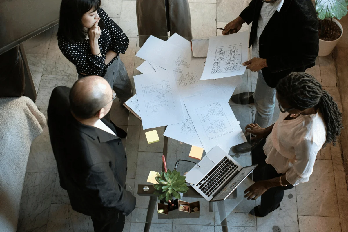 Team reviewing technical drawings around a modern glass table.