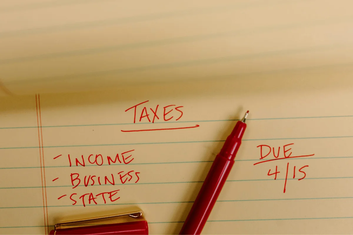 Tax notes written on a legal pad with a red pen listing income, business, and state taxes.