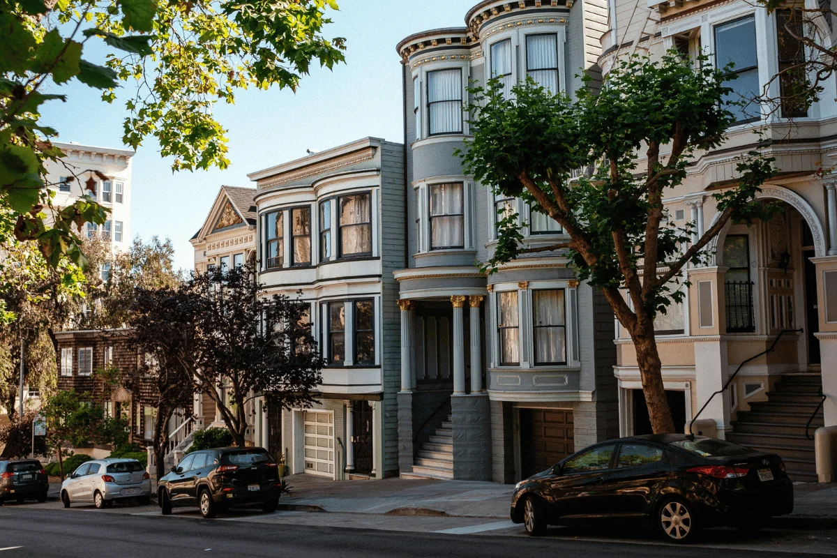 Historic multi-story homes with ornate trim and parked cars in front.