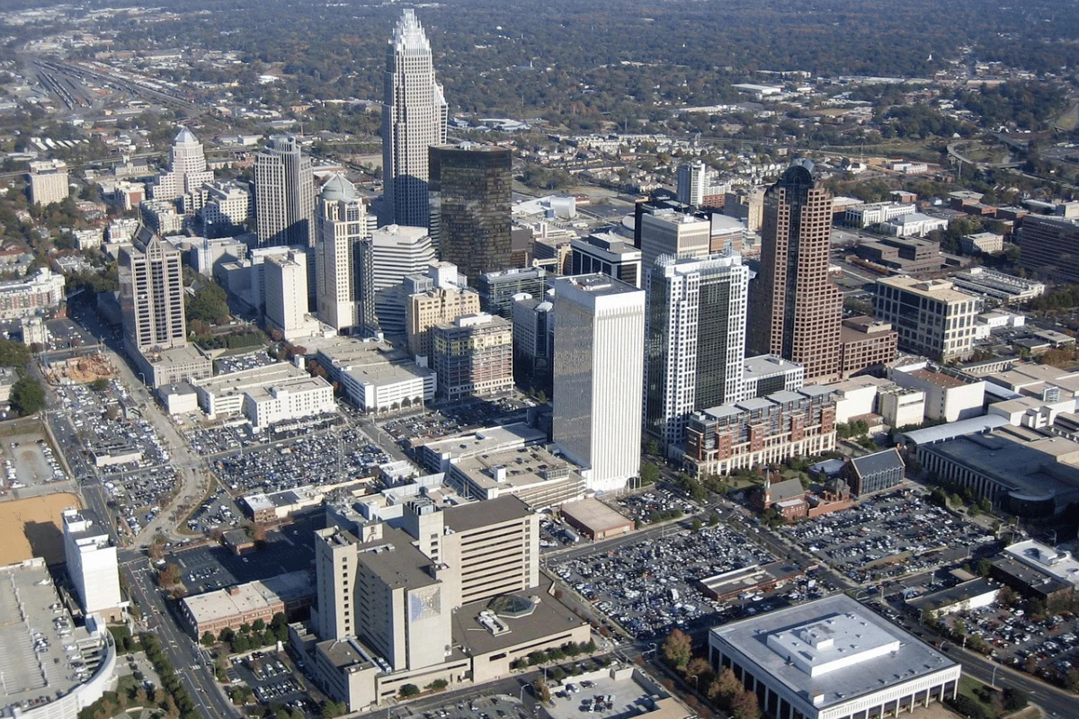 Aerial view of a bustling cityscape with tall skyscrapers, diverse architecture, and surrounding residential areas, set under a clear sky.