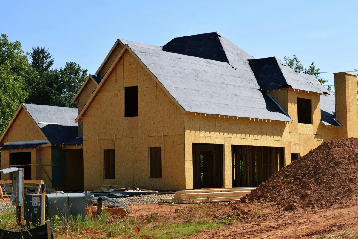 A house under construction with a partially completed roof and walls, with dirt piles nearby.