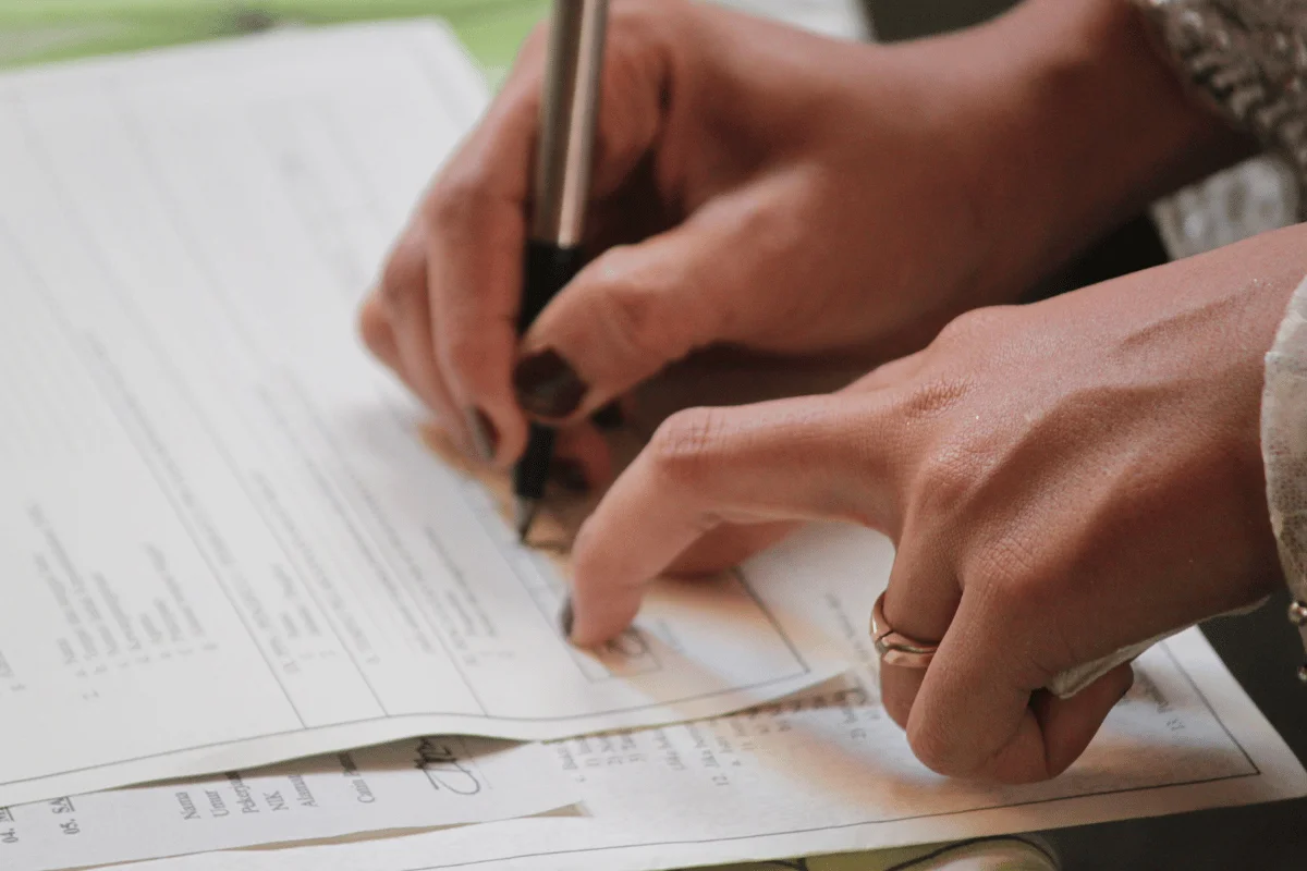 Hands filling out paperwork and writing details on a form at a table.
