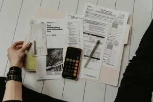 A hand holds a tax document with a calculator and other forms, all laid out on a white wooden surface, preparing for tax filing.