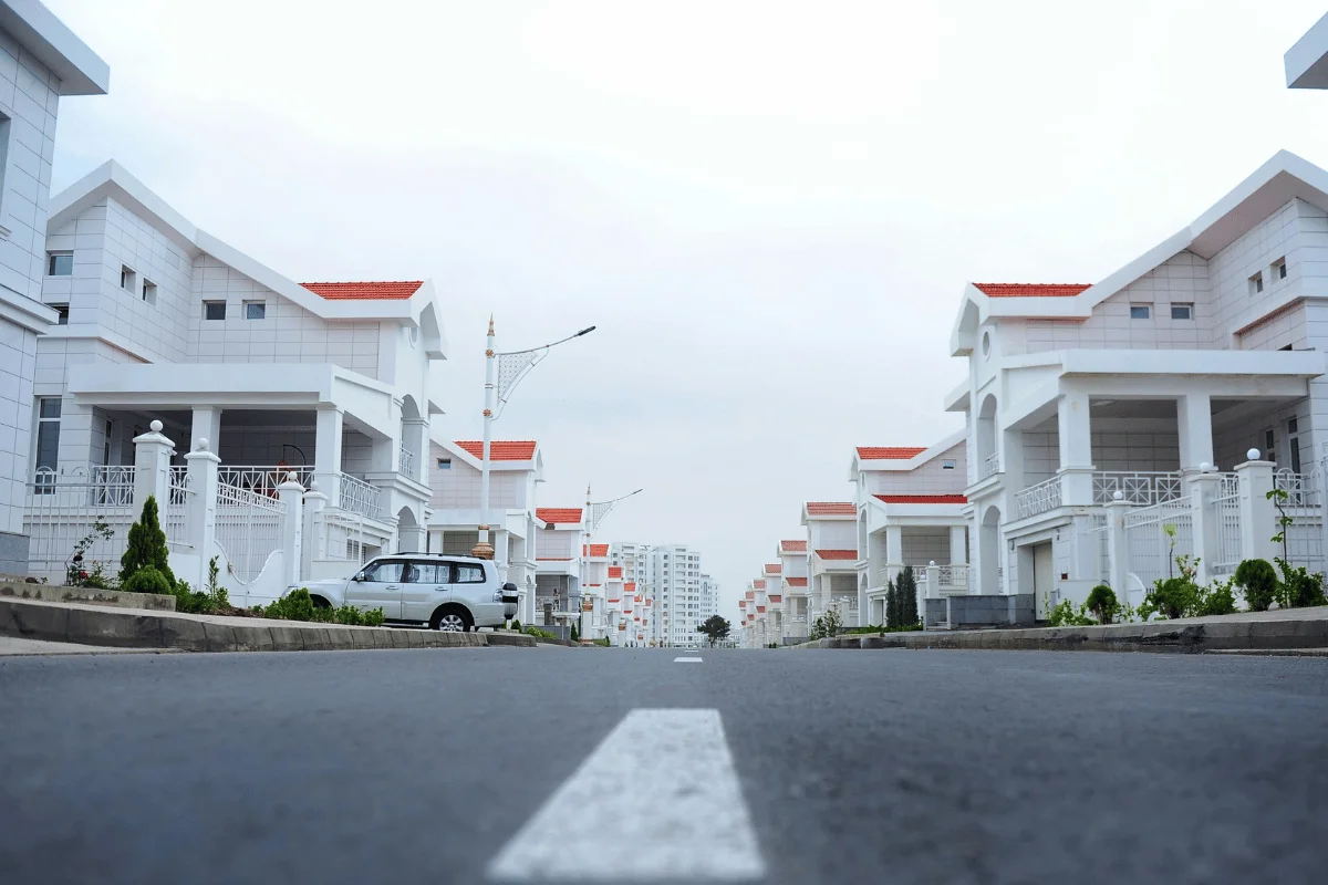 A residential street lined with white houses and a clear sky above.