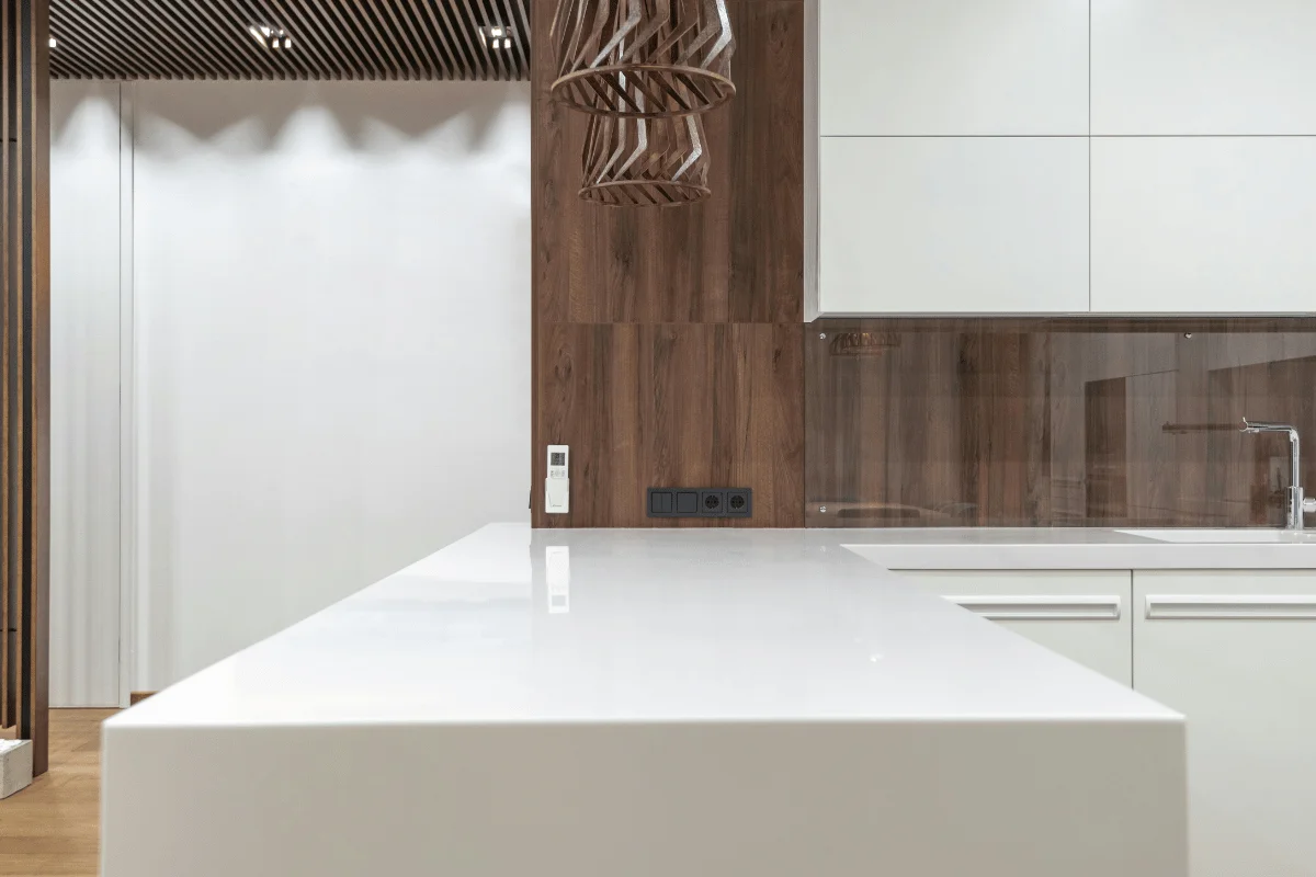 Modern kitchen featuring a sleek white countertop, wooden paneling, minimalist cabinets, and stylish pendant lighting.