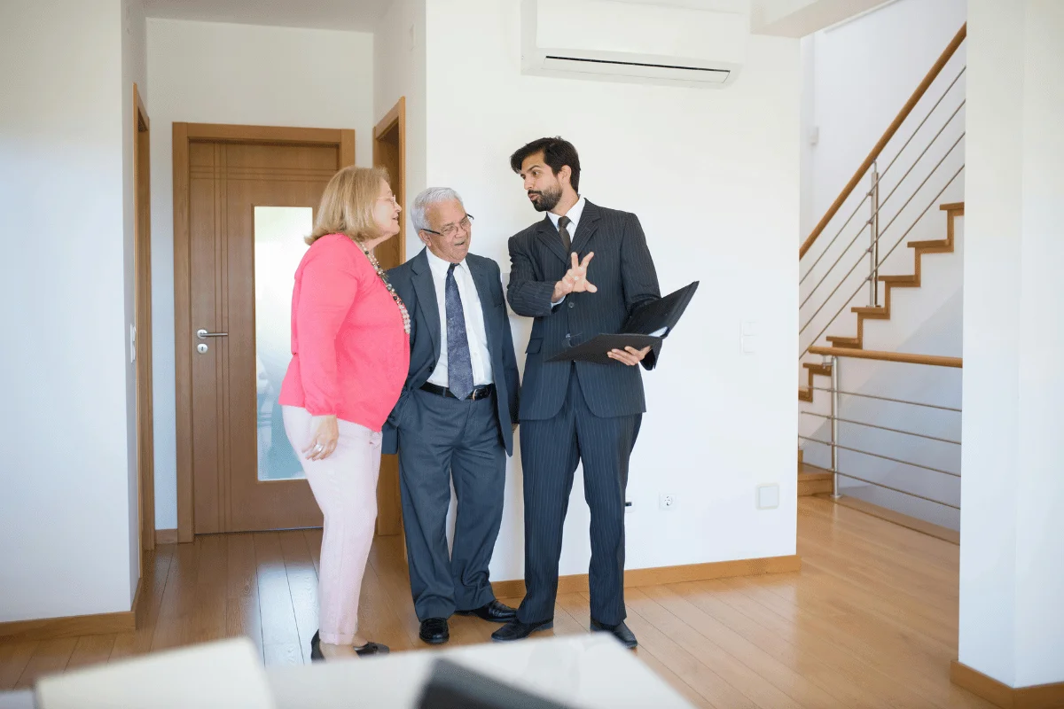 A couple listening to a real estate agent as he explains a property, holding a folder in a modern home.