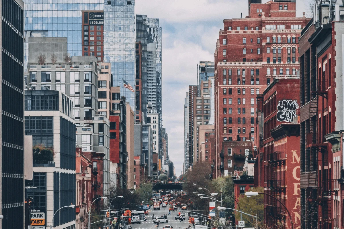A bustling city street flanked by a mix of modern glass buildings and historic brick architecture under a cloudy sky.