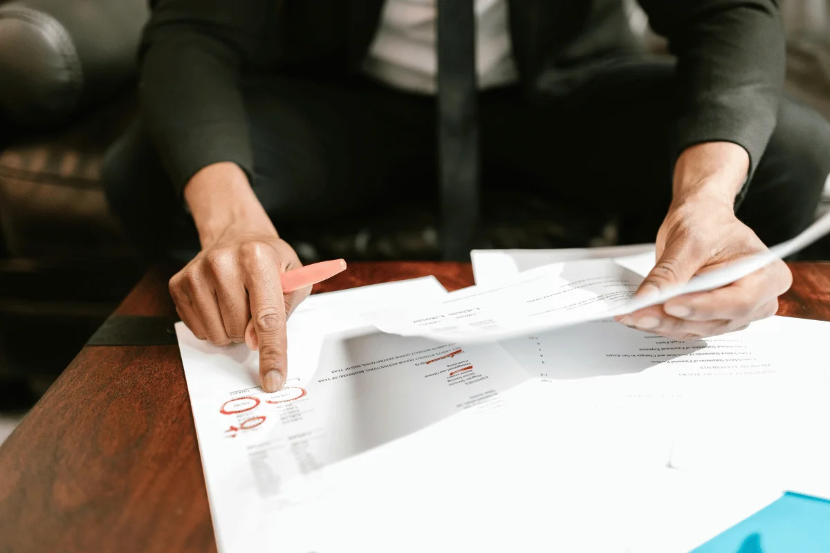 Focused shot of a person marking documents with a pink highlighter and pointing to a section.