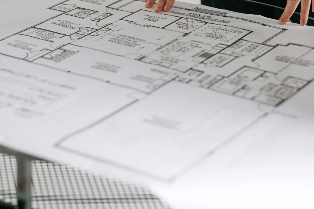 A person’s hands hold a detailed house floor plan, showcasing various rooms and layout on a large sheet of paper.