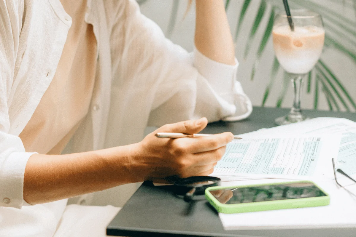 A person in a white shirt is sitting at a table, reviewing documents with a pen.