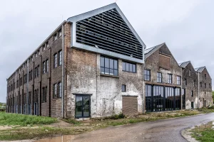Old, weathered brick industrial building with large windows, partially renovated. Overcast sky enhances an atmosphere of urban decay and transition.