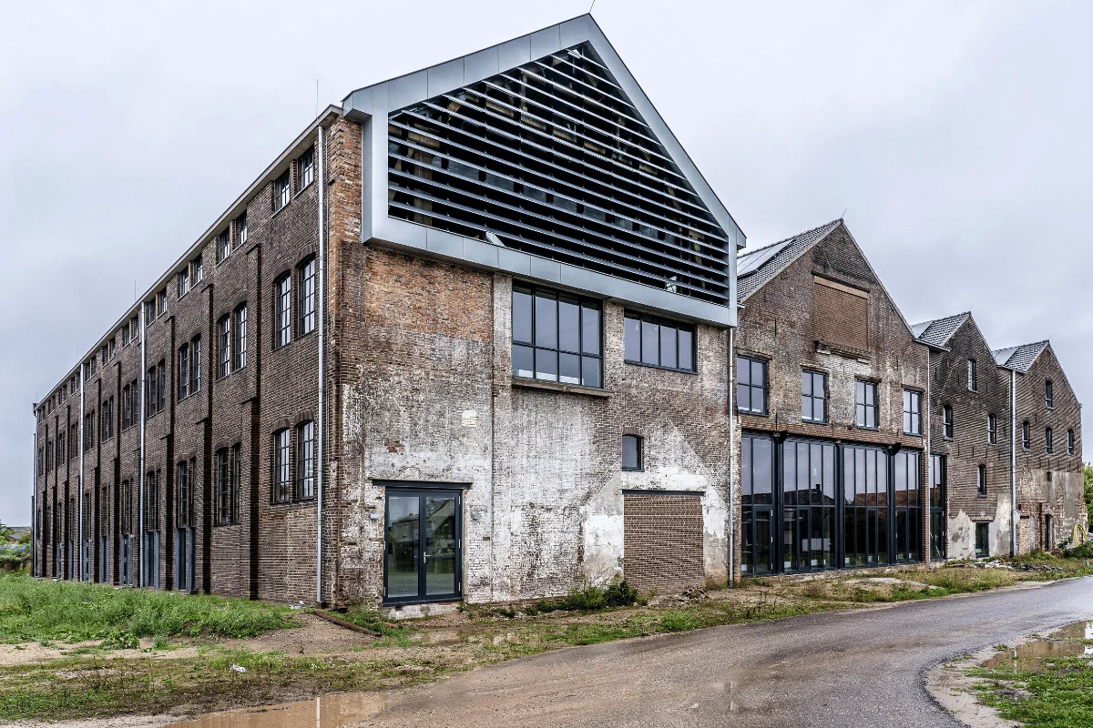 Old, weathered brick industrial building with large windows, partially renovated. Overcast sky enhances an atmosphere of urban decay and transition.