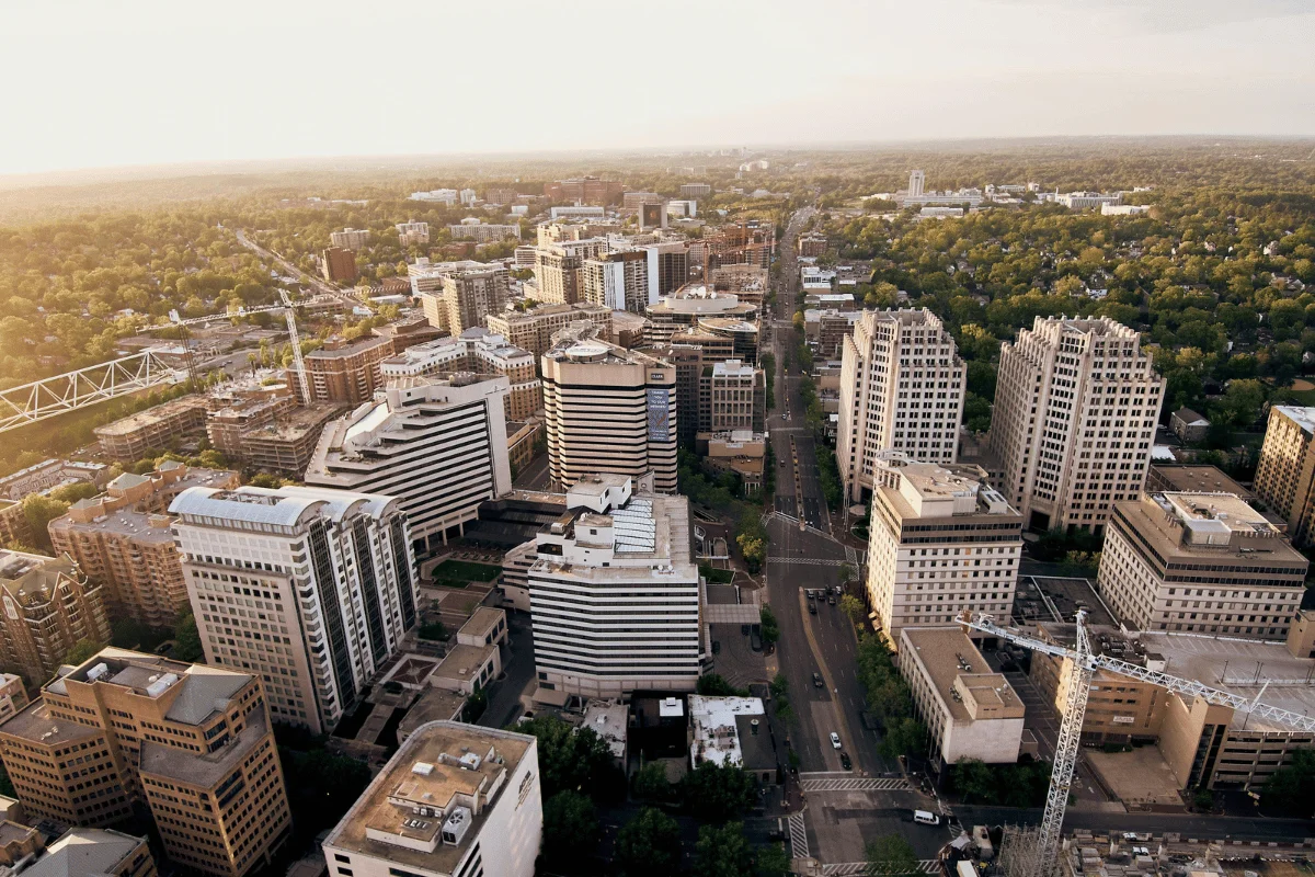 Aerial view of a city skyline featuring modern buildings, streets, and lush greenery in the background during golden hour.