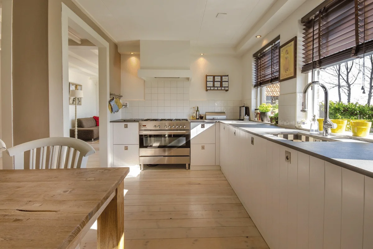 Bright modern kitchen with white cabinets, wooden floors, and stainless steel appliances.