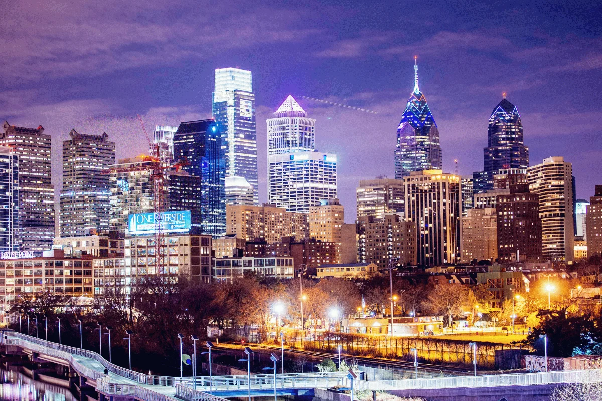 Philadelphia skyline at night, featuring illuminated skyscrapers against a purple sky.