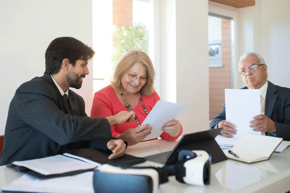 A group of three adults in a well-lit office discuss documents at a table.