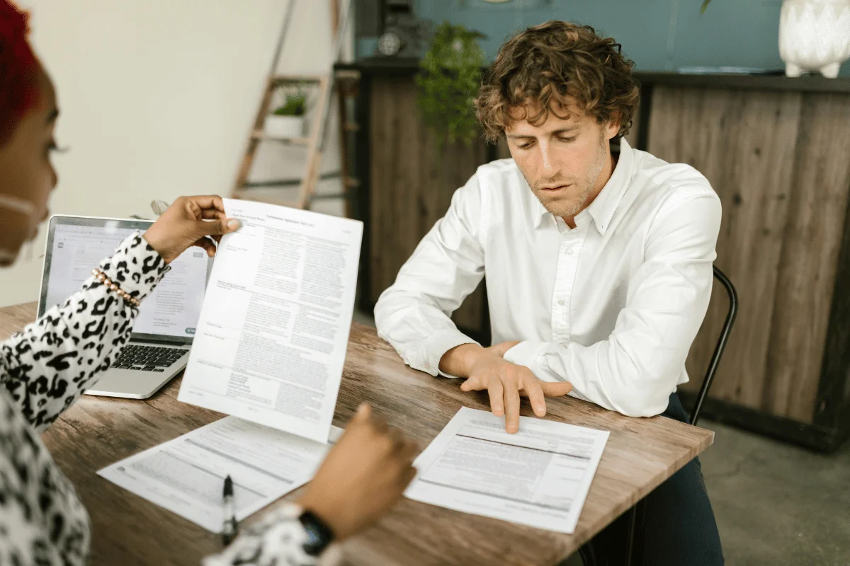 Man reviewing financial documents with a colleague during a meeting at a wooden table.
