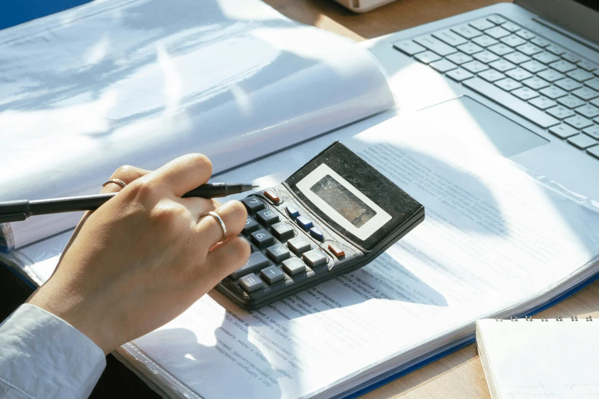 Close-up of hands calculating figures with pen and calculator.