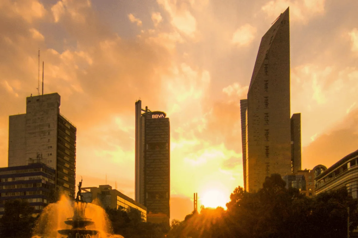 Downtown skyline at sunset with glowing skyscrapers and fountain in the foreground.