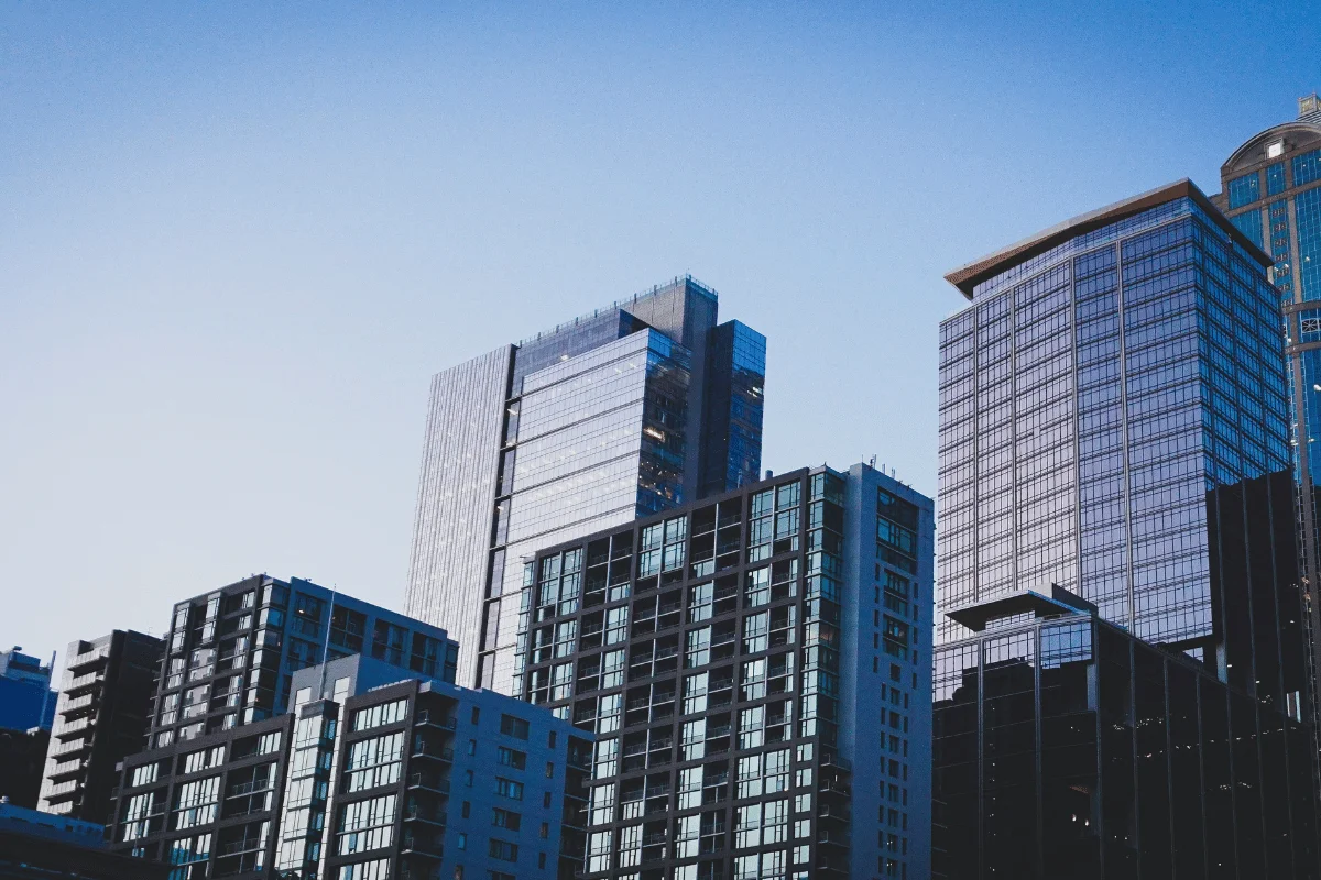 Modern city skyline with glass residential and office towers against a clear blue sky.
