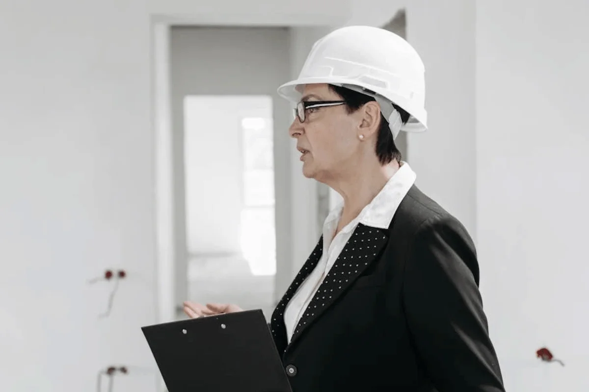 Female construction professional in white hard hat reviewing cost segregation documents in new building interior.