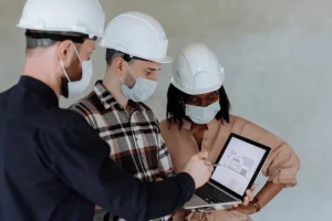 Three construction professionals in hard hats reviewing laptop data for cost segregation new construction acquisition