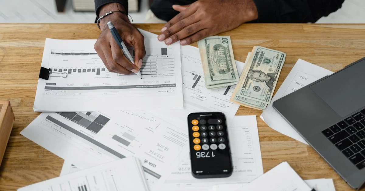 Person conducting cost segregation engineering studies with financial documents, calculator, cash, and laptop on desk.