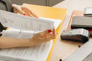 A person with red nail polish flips through documents in a binder at a desk.